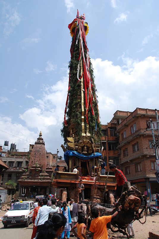 Kathmandu Patan 03 Rato Machhendranath Chariot The Rato Macchendranath wooden-wheeled chariot sad idle in the street of Patan waiting to be moved later in the day. It has a very unwieldy tall spire made from bamboo poles raised from four ends of the chariot, making the chariot balance precariously. Rato (Red) Macchendranath is the god of rain and plenty, and is a tantric version of Avolokiteshvara to Buddhists and a version of Shiva to Hindus. This is the longest and most important festival of Patan, beginning with building the chariot, and then towing the chariot through the streets of Patan every day for a month, ending just before the monsoon.